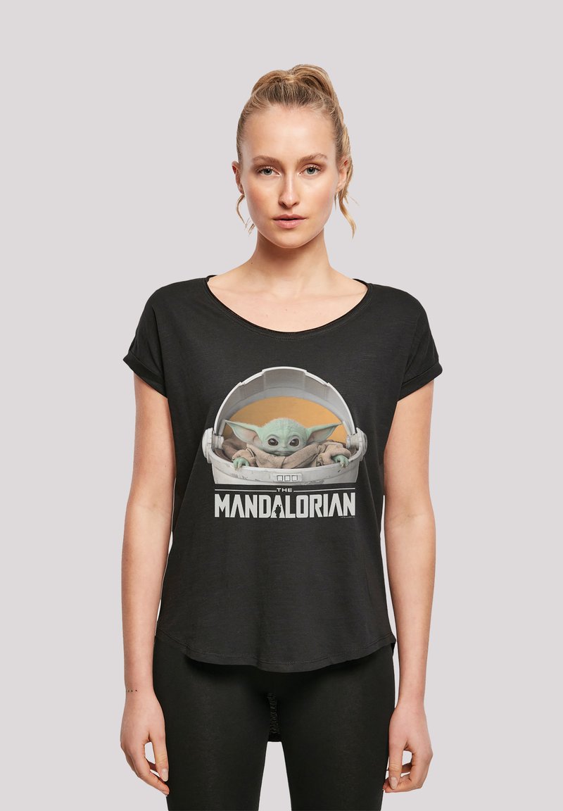 Svart t-skjorte laget av mykt stoff med et grafisk motiv av en karakter i en pod, med teksten "THE MANDALORIAN" under. Korte ermer, avslappet passform.