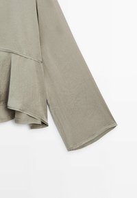 Haut gris clair avec un design fluide, caractérisé par des manches larges et un ourlet en couches. Confectionné dans un tissu doux et texturé.
