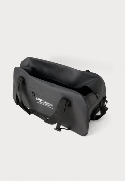Borsa impermeabile nera con manici robusti e superficie texturizzata. Presenta una tasca con zip e un dettaglio del logo sul fronte.