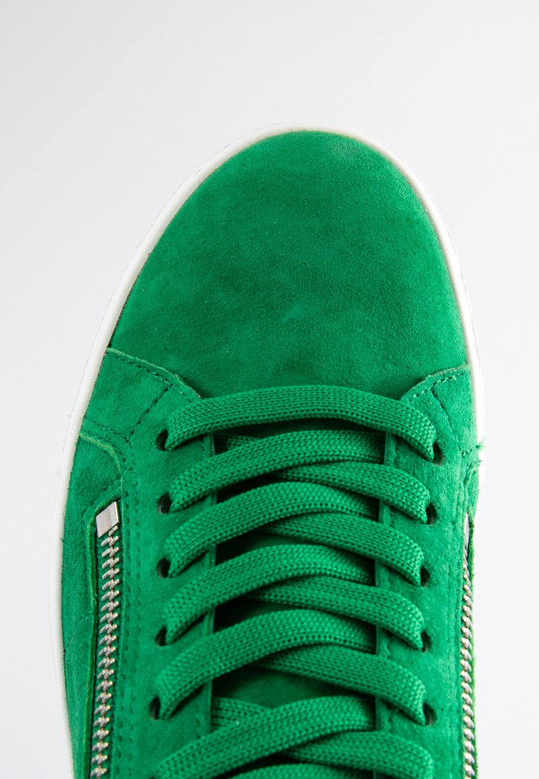 Grüne Wildleder-Sneaker mit strukturiertem Obermaterial, weißer Gummisohle, kontrastierenden Schnürsenkeln und metallic Reißverschlussdetail an der Seite.