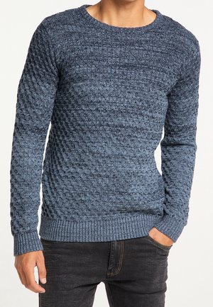Maglione blu a trama con scollo rotondo e polsini a costine. Motivo sfumato su tutta la superficie, realizzato in tessuto a maglia, abbinato a jeans scuri.