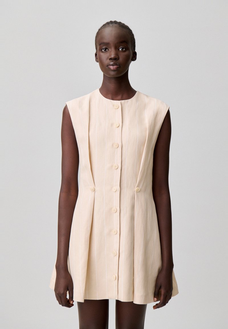 Vestido corto sin mangas en beige claro con finas rayas verticales, con escote redondeado y seis botones en la parte delantera.