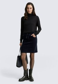 Czarny golf, granatowa spódnica sztruksowa ze sznurkiem, czarna torba typu tote, przezroczyste czarne rajstopy i czarne botki za kostkę. Prosty, dopasowany fason.