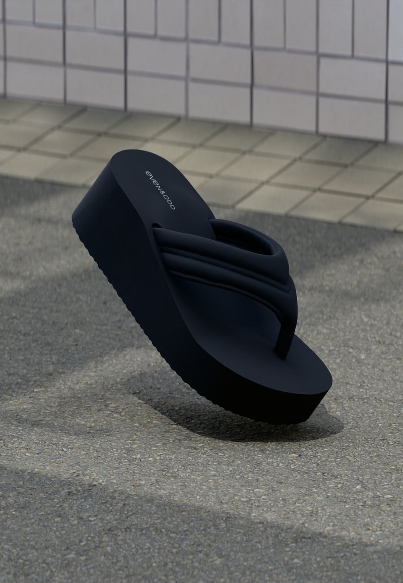 Μαύρο πλατφόρμα σαγιονάρα με επενδεδυμένους ιμάντες, τοποθετημένη σε γωνία πάνω σε υφή εδάφους με φόντο τοιχο από πλακάκια.