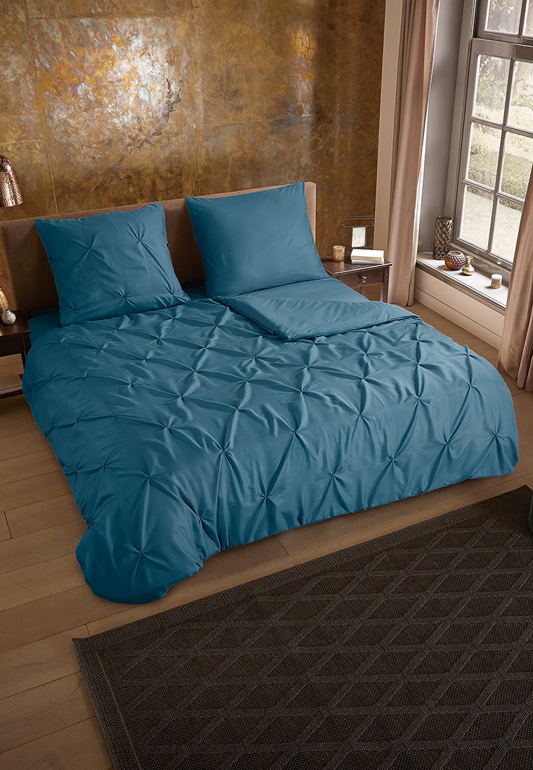 Teal-Bettwäsche-Set mit einem strukturierten, gesteppten Design, umfasst zwei Kissenbezüge und ein Bettlaken, ordentlich auf einem Holzbettgestell arrangiert.