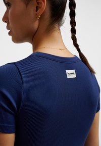 Granatowy prążkowany top z krótkim rękawem, z kwadratową etykietą "hummel PERFORMANCE" na plecach, teksturowaną tkaniną i dopasowanym krojem.