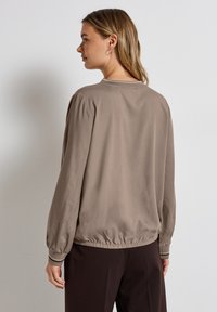 Haut marron à manches longues avec un col rond, des épaules froncées et un ourlet élastiqué. Tissu doux et lisse avec une coupe décontractée.