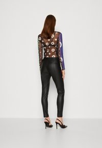 Pantaloni in pelle nera abbinati a una blusa trasparente a maniche lunghe con motivo floreale e maniche multicolori, dal design aderente.