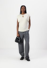 Haut créme à manches courtes avec un détail en forme de trou de serrure au niveau du col, associé à un pantalon large gris. Un sac à main noir complète le look.