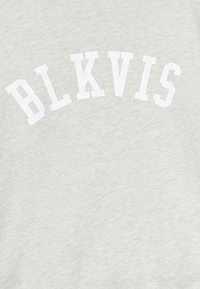 Białe litery blokowe układające się w łuk z napisem "BLKVIS" na tle jasnoszarej tkaniny z efektem heather.