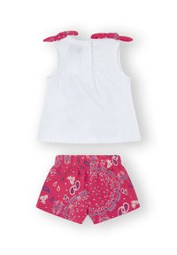 Top blanco sin mangas con dos lazos rojos estampados en los hombros, combinado con pantalones cortos rojos que presentan diseños florales y de paisley en blanco.