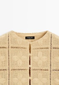 Beżowy kardigan z dzianiny na szydełku z kwiatowymi wzorami, okrągłym dekoltem, czterema guzikami z przodu oraz metką Massimo Dutti wewnątrz kołnierza.