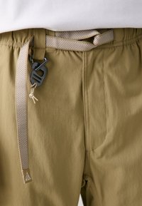 Elastic waist cargo pants in olive green, featuring a textured fabric, woven beige belt, and black metal hardware detail.