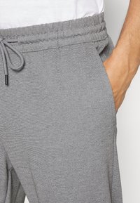 Midja och överlår på en person som bär ljusgråa sweatpants med elastisk midja och dragsko, hand vilande i höger ficka.