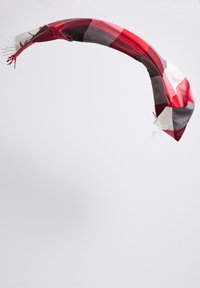 Écharpe à carreaux rouge, grise et blanche en tissu doux, avec des bords à franges et un design léger et fluide.