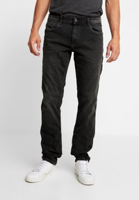 Jeans de mezclilla negra con un ajuste slim, diseño de cinco bolsillos, un ligero desvanecimiento y una cintura estándar, combinados con zapatillas blancas.