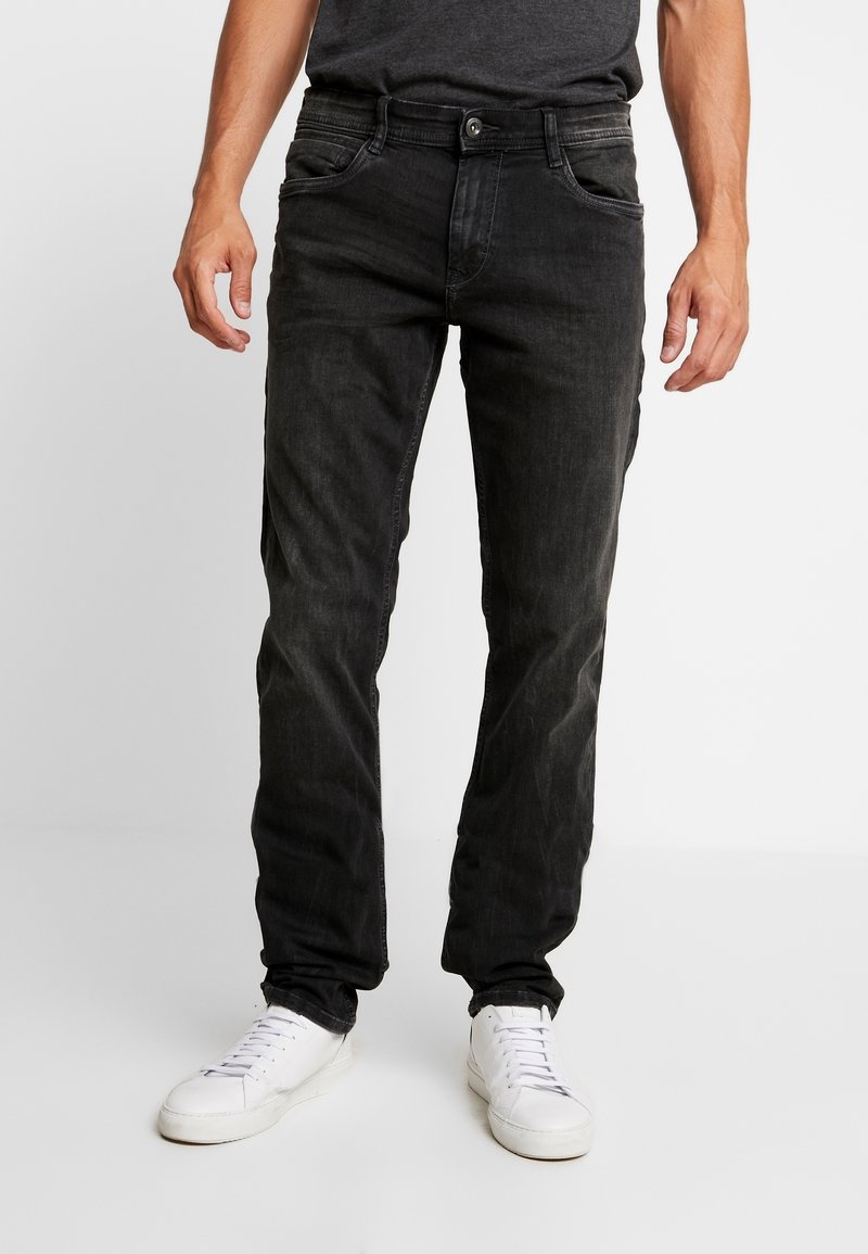 Jeans de mezclilla negra con un ajuste slim, diseño de cinco bolsillos, un ligero desvanecimiento y una cintura estándar, combinados con zapatillas blancas.