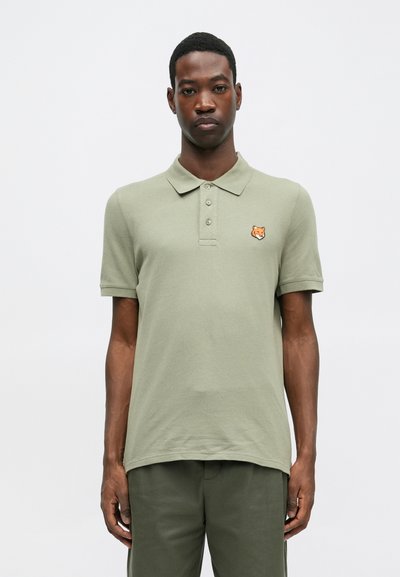 Kaki polo majica s kragnom, kratkim rukavima, trojbatnim patentom i izvezenim logotipom lisice na lijevoj strani prsnog koša. Mekani pamučni materijal.