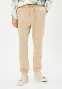 Pantalones jogger beiges con cintura elástica y cordón. Tejido suave con un corte relajado, que presenta puños en los tobillos y bolsillos laterales.