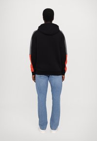 Felpa con cappuccio nera con maniche color block grigie e rosse, realizzata in tessuto morbido. Abbinata a jeans di denim azzurri e scarpe da ginnastica bianche.