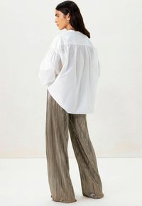 Witte, losse blouse met gepofte mouwen, gecombineerd met glanzende, geplooide, brede broek in een metallic bronzen tint.