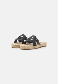 Svart läder slip-in sandaler har utskärningar, beigemönstrad espadrillesula och silvernitar på sidorna för extra detalj.