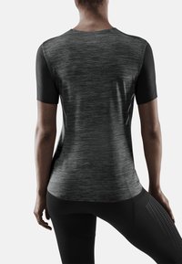 Camiseta deportiva de manga corta en negro y gris con tejido texturizado, escote redondo y mangas negras en contraste, combinada con leggings negros que presentan acentos estampados.