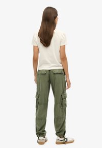 Pantalons cargo verts avec plusieurs poches, poignets élastiques et coupe décontractée, associés à un t-shirt blanc uni et des baskets décontractées.