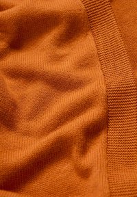 Bränd orange stickad tyg med en strukturerad yta, som har en slät, mjuk väv och en ribbad accent längs en kant.