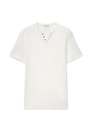 T-shirt bianca semplice a maniche corte con scollo rotondo caratterizzato da un piccolo taglio a V e quattro bottoni scuri sul lato sinistro.