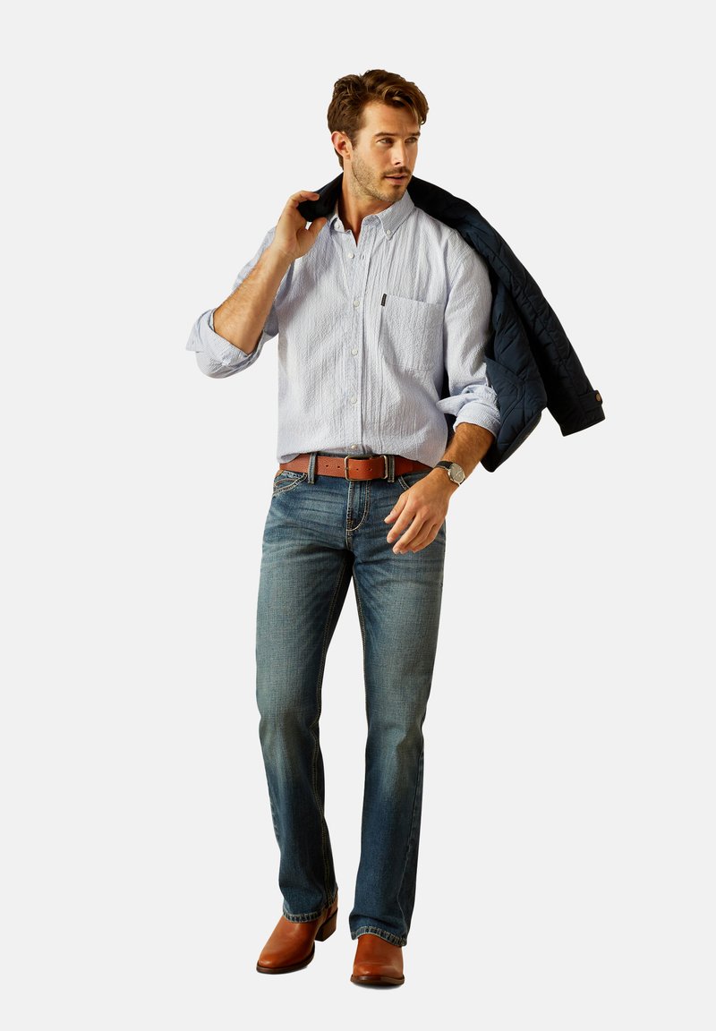 Light blue striped button-up shirt, dark jeans, brown belt, brown dress boots; holding a navy jacket over shoulder.