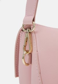 Rosa läderhandväska med guldfärgad hårdvara och en klämma. Har sömnadsdetaljer och en rundad form för enkel hantering.