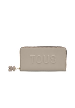 Billetera rectangular beige con cremallera que rodea, con el logo "TOUS" en relieve y un pequeño tirador de cremallera en forma de oso en el lado izquierdo.