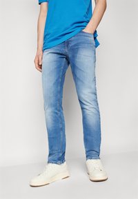 Light blue denim jeans with a slim fit, featuring a slightly distressed texture and front pockets. Paired with white sneakers.