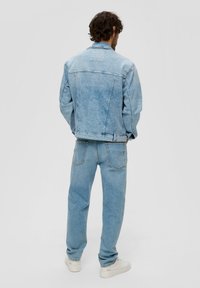 Jasnoniebieska dżinsowa kurtka o luźnym kroju, z widocznym szyciem i bocznymi kieszeniami, połączona z pasującymi jasnoniebieskimi dżinsami i białymi trampkami.