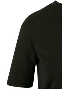 Gros plan d'un t-shirt noir à manches courtes montrant la texture du tissu, la couture de l’épaule et l’ourlet de la manche sur un fond blanc uni.
