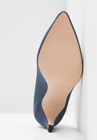 Chaussure à talon haut bleu marine avec bout pointu, dessus en textile lisse, et semelle plate de couleur claire. Présente un design profilé et élégant.