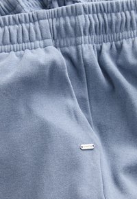 Pantalon de survêtement bleu clair en tissu côtelé avec une taille élastique et une petite étiquette argentée embossée du mot "DOWNTIME".