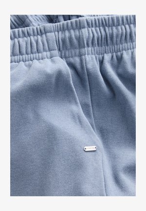 Helesinised dressipüksid, valmistatud soonikkoes kangast, millel on elastne vöökoht ja väike hõbedane silt, millele on reljeeftrükitud "DOWNTIME".