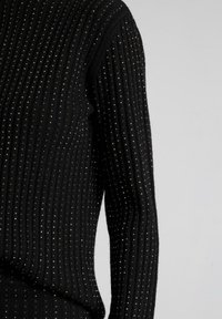 Zwarte geribde sweater met een textuurstof en kleine metalen accenten. Strak ontwerp met lange mouwen, dat warmte en detail benadrukt.