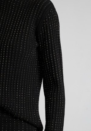Maglione nero a coste con un tessuto testurizzato e piccoli accenti metallici. Design aderente con maniche lunghe, che enfatizza il calore e i dettagli.