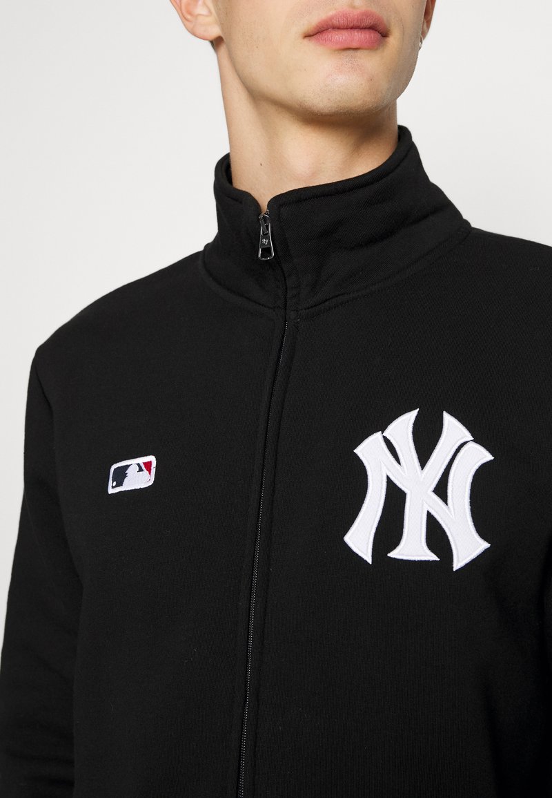 Black zip-up sweatshirt made from soft fabric featuring a white embroidered New York Yankees logo on the chest and a small MLB logo patch.