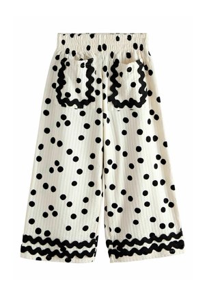 Baltas īssiksnas ar melniem polka punktiņiem, elastīgu jostasvietu, divas aizmugures kabatas ar melnu viļņotu apmalu un saskaņotu apmali apakšā.