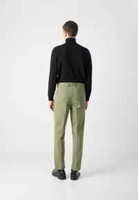 Maglietta nera a maniche lunghe abbinata a pantaloni verde chiaro, con tasche laterali e vestibilità slim, completata da scarpe nere.