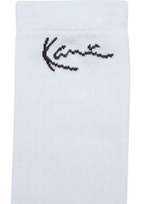 Hvide bomuldsstrømper med et tekstureret strikkemønster og et sort broderet logo på siden. Enkel design med en ribbet kant.