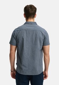 Camisa de manga corta con cuello en rayas verticales azul marino y blanca. Presenta un corte relajado y una textura suave, con un sutil diseño en el yugo trasero.