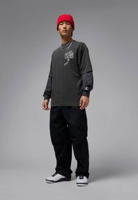 Gray long-sleeve shirt with a graphic print, layered over a black long-sleeve shirt, paired with black cargo pants and white sneakers. Red beanie.