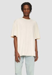 Crème-kleurig oversized t-shirt van zachte katoen jersey met korte mouwen. Gecombineerd met lichtblauwe versleten jeans. Eenvoudig ontwerp, geen patronen.