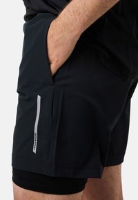 Mustat urheilushortsit, joissa on sileä pinta, sivutasku sekä heijastava valkoinen raita etuosassa. Alhaalla näkyy tiukka pohjakerros.