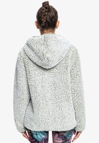 Lys grøn, struktureret fleecejakke med hætte, der har en løs pasform og sænkede skuldre. Blød, fluffy overflade uden synlige lukninger.